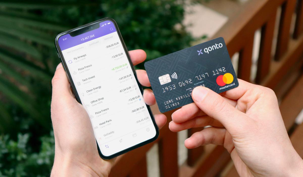 Main d’une personne tenant sa carte de crédit Qonto et son smartphone y compris un compte ouvert.